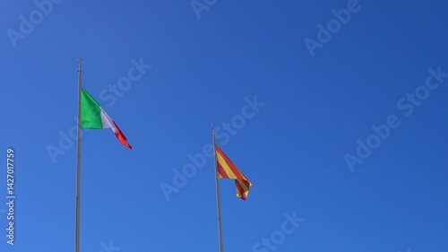 Two flags fluttering in the wind on tall poles with deep blue sky in the background on a sunny day