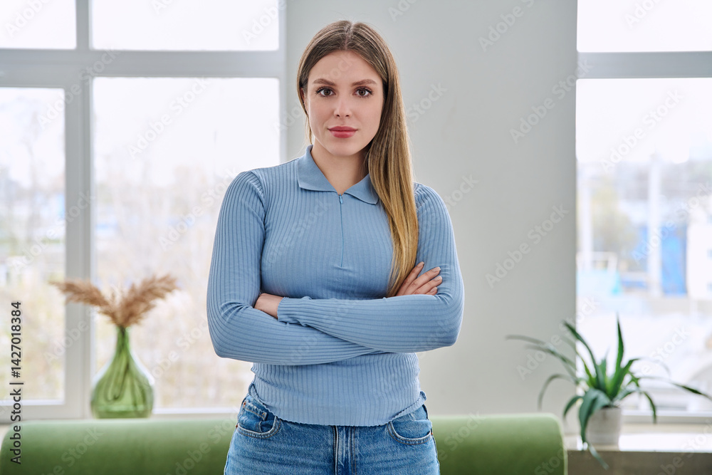 Portrait of confident young woman posing with crossed arms in home interior
