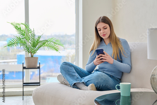Young woman sitting at home in chair using smartphone