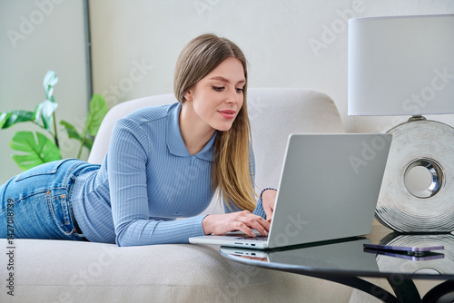 Obraz na płótnie Young woman lying on sofa at home using laptop w salonie