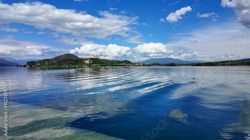 Peaceful lake with soft waves, hillside town and bright sky with clouds seen from across the water