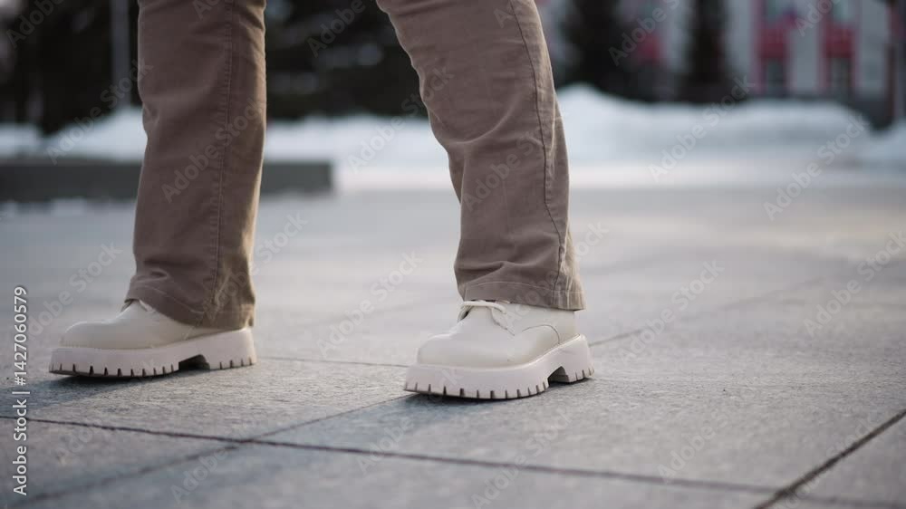 Leg view of young lady dancing on tiled outdoor floor wearing corduroy trousers and canvas boots capturing rhythmic motion against urban pavement with winter light and snow backdrop