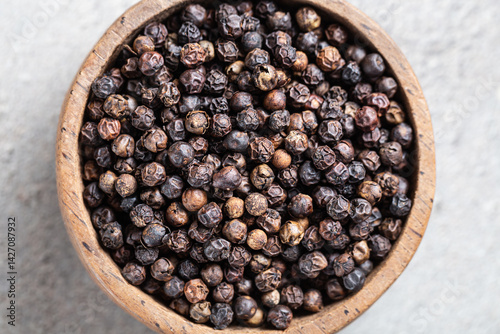 Fototapeta Naklejka Na Ścianę i Meble -  Indian spice black pepper in wooden bowl close-up on gray background macro shot. Hot spices. Herbal alternative Ayurvedic medicine. 