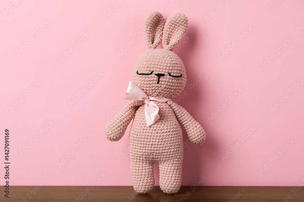 Cute knitted toy bunny on wooden table against pink background
