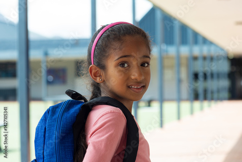 Obraz na płótnie Girl child standing in covered school corridor, wearing pink headband and carrying blue backpack w salonie