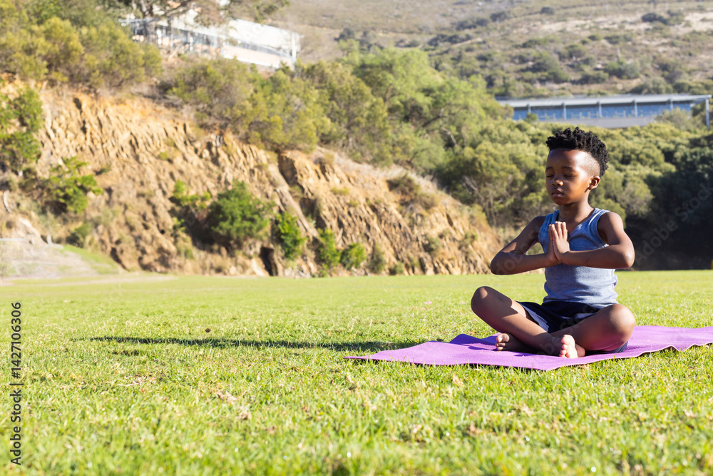 African American boy meditating on pink yoga mat in public park, finding calm focus, copy space