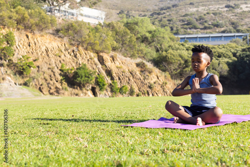 Obraz na płótnie African American boy meditating on pink yoga mat in public park, finding calm focus, copy space w salonie