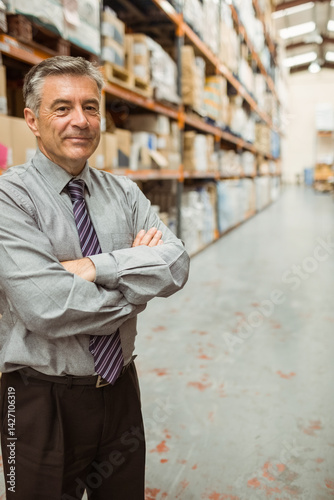 Obraz na płótnie Mature man standing with arms crossed in warehouse aisle, with metal shelves and boxes, copy space w salonie