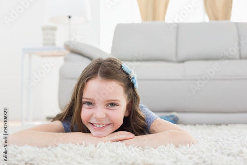 female child lying on stomach on white fluffy rug in living room with blue hair bow