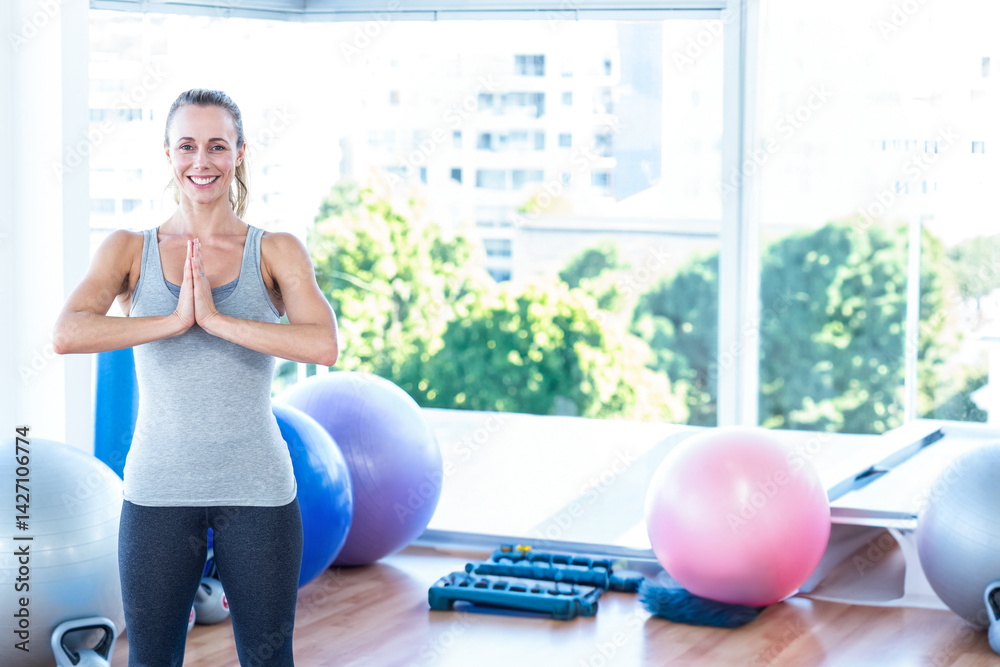 Woman holding yoga prayer pose in fitness studio, with stability balls and dumbbells, copy space