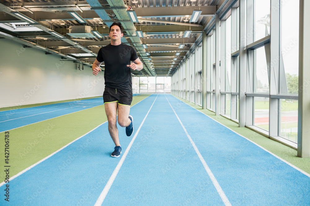 Young adult male athlete sprinting on synthetic track in training facility, with running shoes