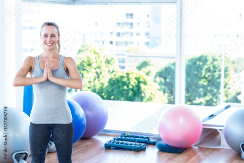 Woman holding yoga prayer pose in fitness studio, with stability balls and dumbbells, copy space