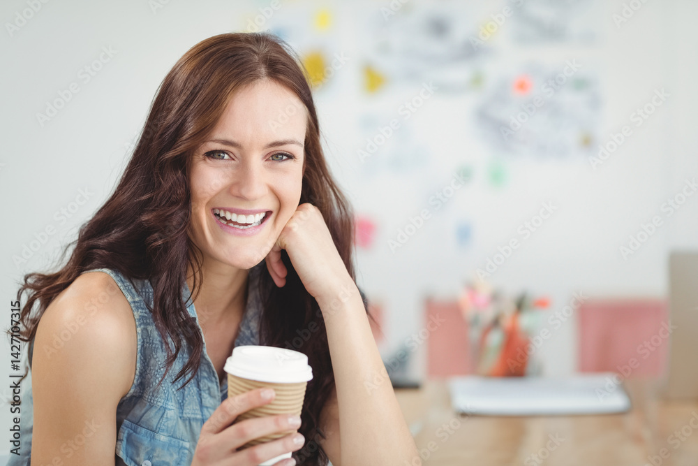 Young woman holding coffee cup, smiling at camera in office at table with whiteboard, copy space