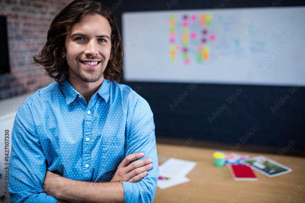 Man standing crossing arms and smiling in modern office, with whiteboard and coffee cup