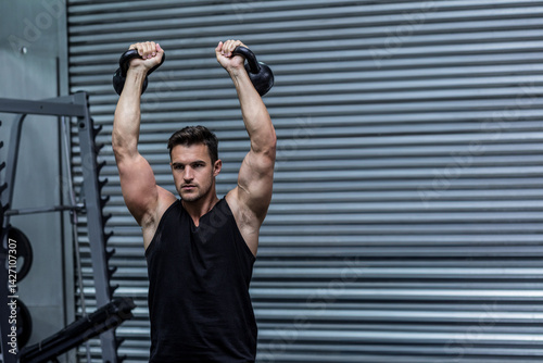 Obraz na płótnie Man lifting kettlebells overhead at industrial-style gym, with weight rack and rubber flooring w salonie