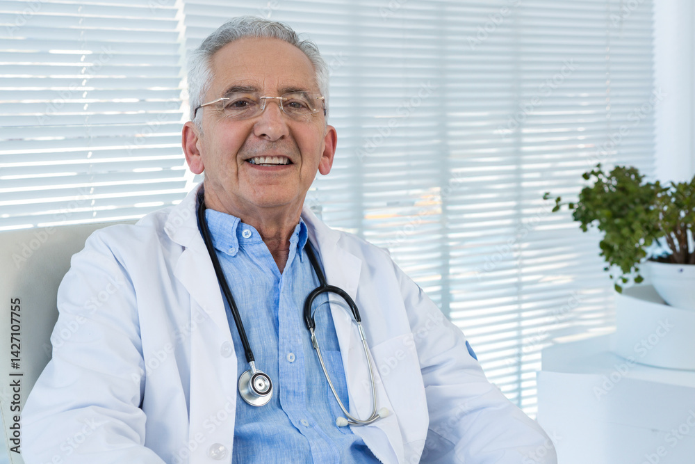 Senior doctor sitting in medical office by window blinds, wearing lab coat, stethoscope, copy space