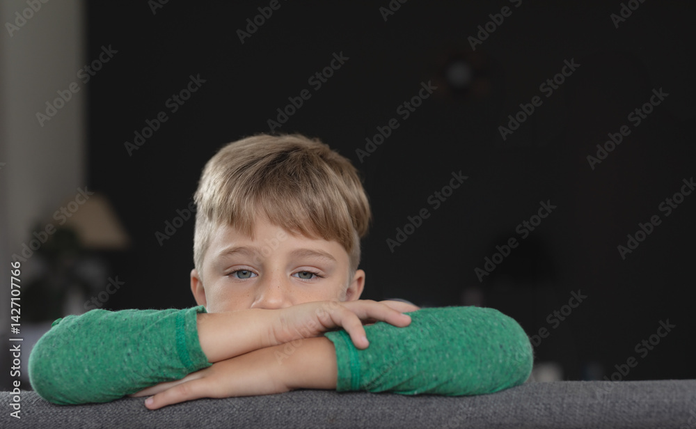 Boy leaning on gray couch back in living room, surrounded by table lamp and potted plant