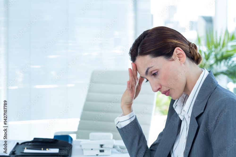 Mid adult businesswoman sitting at office desk, leaning head on hand with phone, papers, copy space