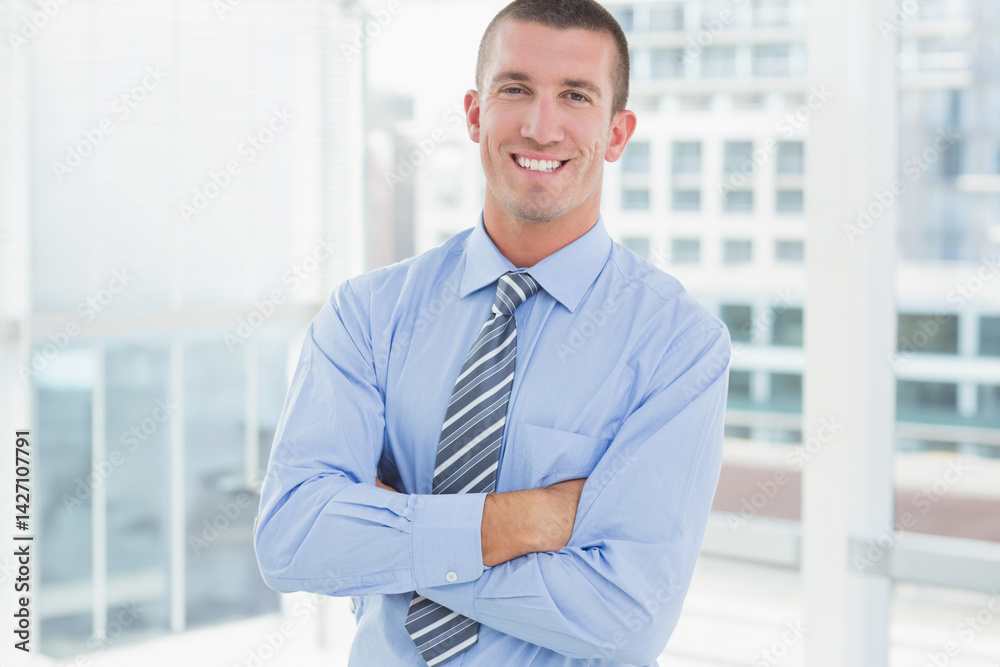 Man standing smiling crossing arms in office with dress shirt, striped necktie and windows
