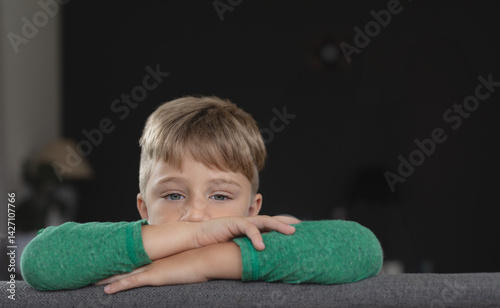 Obraz na płótnie Boy leaning on gray couch back in living room, surrounded by table lamp and potted plant w salonie