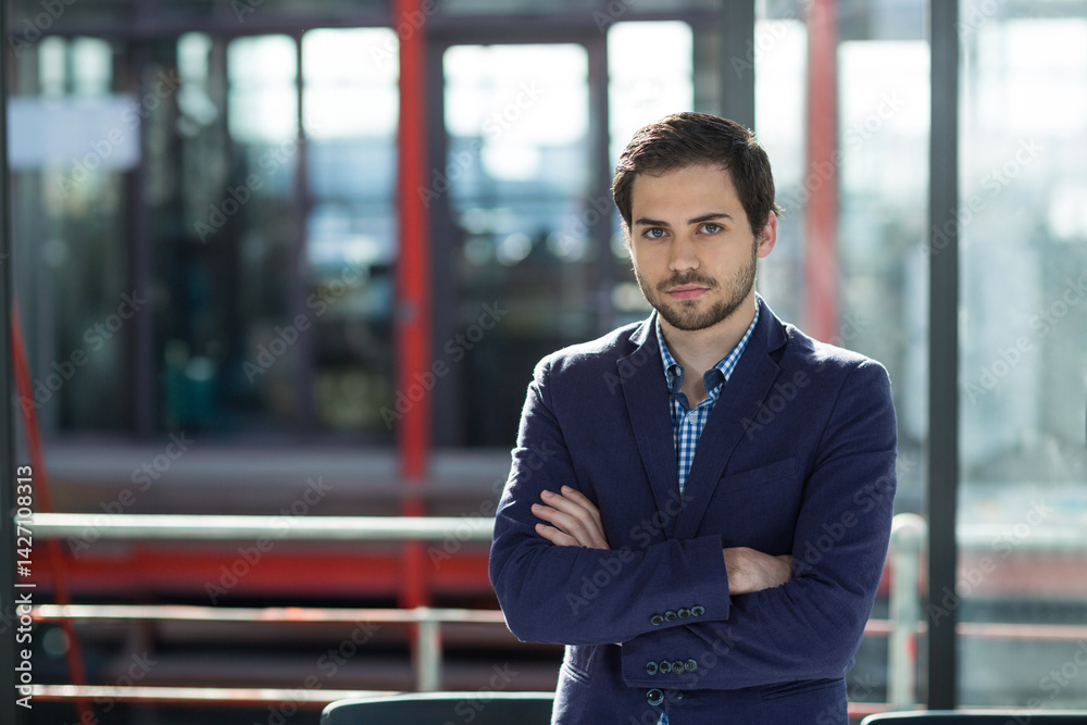 Man standing with arms crossed in modern office lobby, metal railing and red beams, copy space