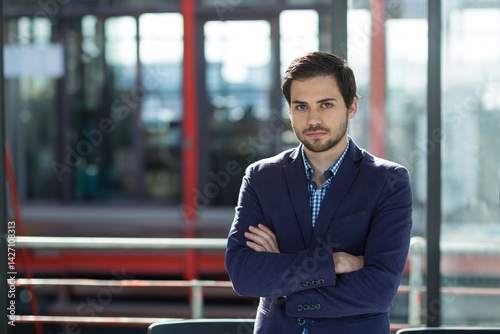 Obraz na płótnie Man standing with arms crossed in modern office lobby, metal railing and red beams, copy space w salonie