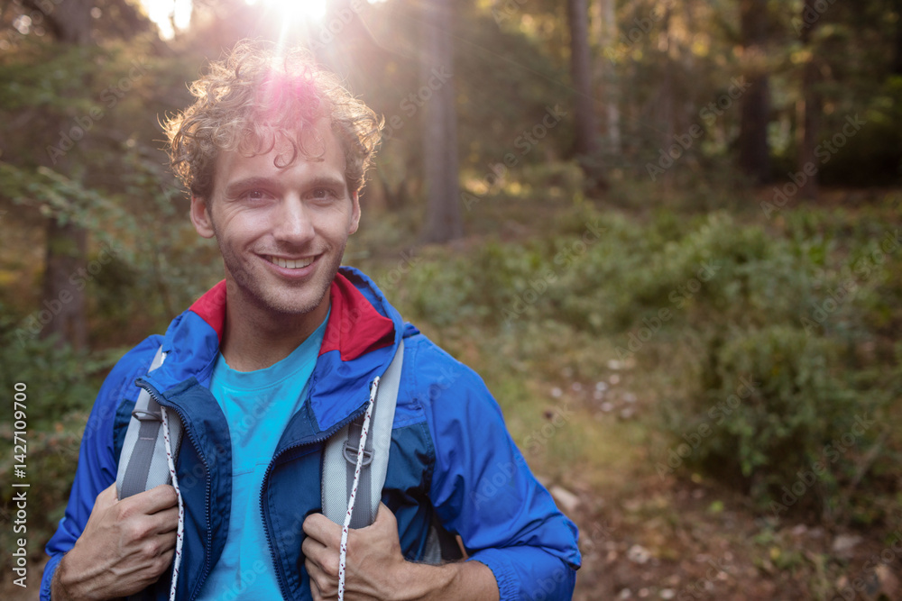 Man in mid twenties hiking forest trail in late afternoon with blue jacket, backpack, copy space