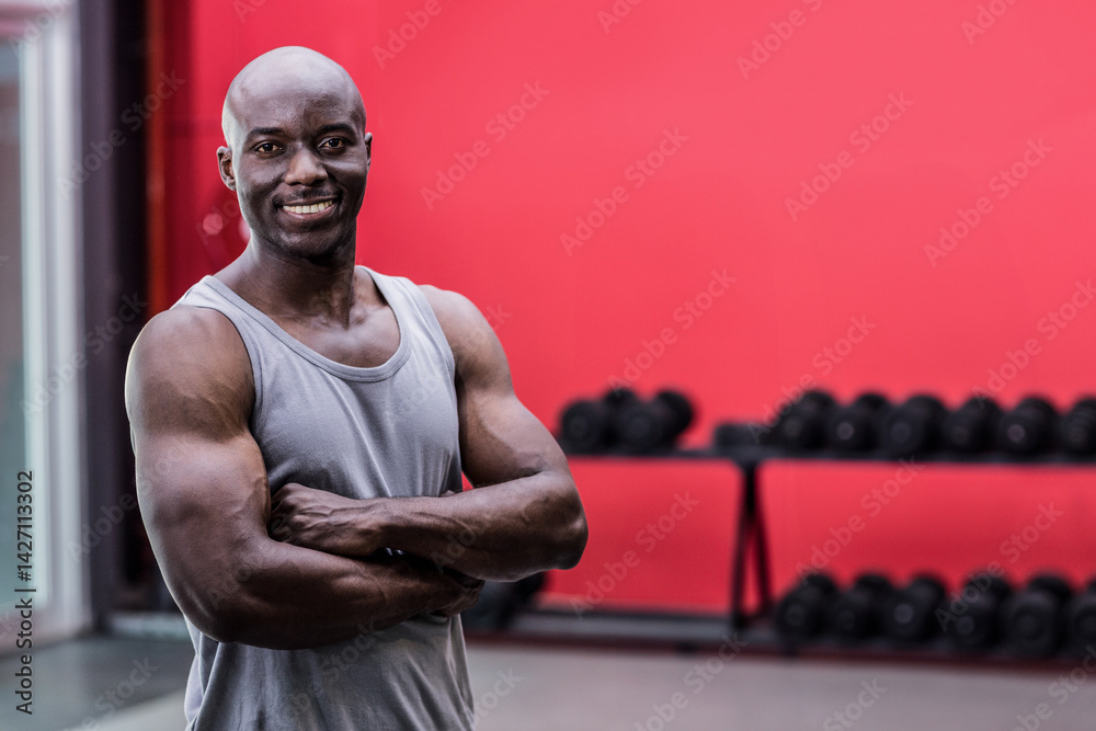African American man standing with arms crossed in gym, with rack of black dumbbells, copy space