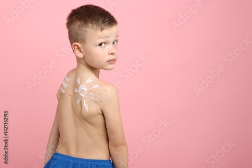 Little boy with sun protection cream on his skin against pink background, space for text