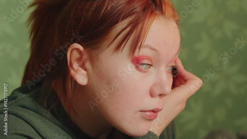 A young woman is focused on applying vibrant eyeshadow while looking into a mirror