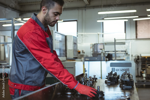 Middle Eastern man inspecting machined metal parts on workbench in CNC machine shop, copy space