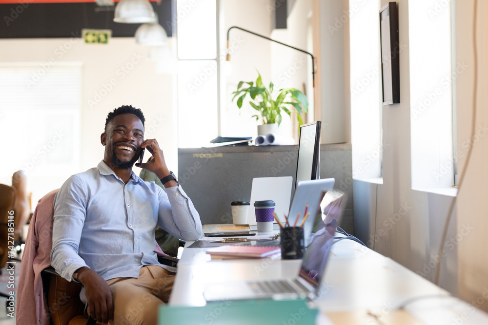 © Wavebreak Media - African American man sitting at desk in modern office, holding smartphone and looking at laptops © Wavebreak Media - African American man sitting at desk in modern office, holding smartphone and looking at laptops