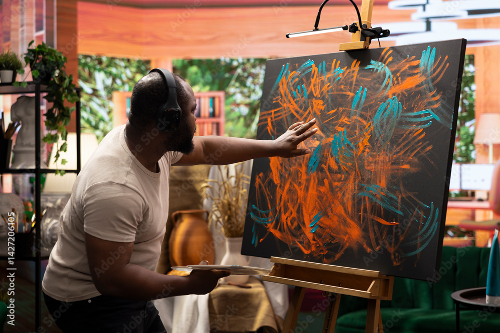 Artist listening to music and creating an abstract painting with his fingers, showing his skills and contemporary ideas in art studio. Creative process finger painting for vibrant artwork.