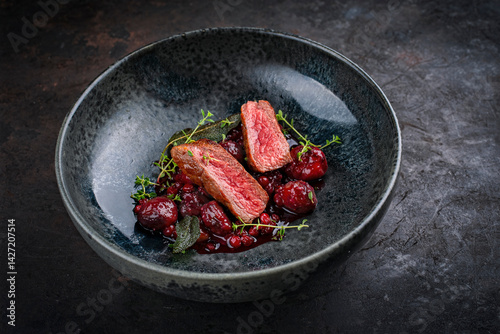 Traditionally roasted fillet of saddle of venison with chestnuts, bacon-wrapped bean sticks and redcurrants served with lingonberry sauce as close-up in a bowl with a rustic background