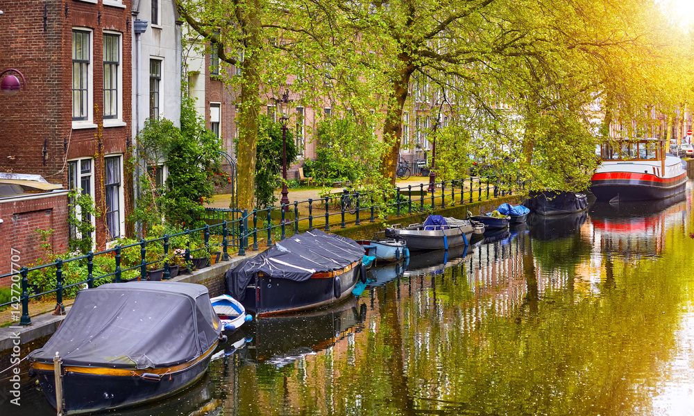Netherlands Amsterdam. View at river Amstel with traditional houses at bank and boats at water canal. Scenic cityscape. Spring day.