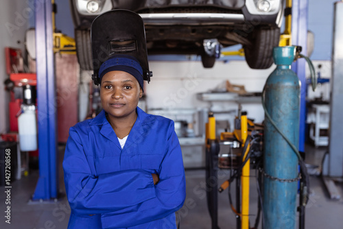 African American female standing in garage with welding helmet flipped up near hydraulic lift