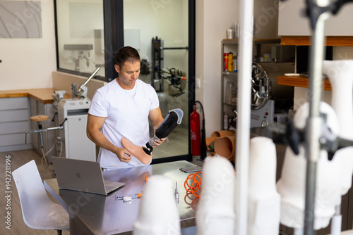 Male technician inspecting below-knee prosthetic leg on workbench in prosthetics workshop photo