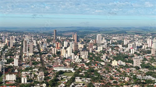 Aerial panoramic view of Cascavel, Paraná, Brazil, featuring a dense skyline of residential and commercial buildings surrounded by rural landscapes in the background.