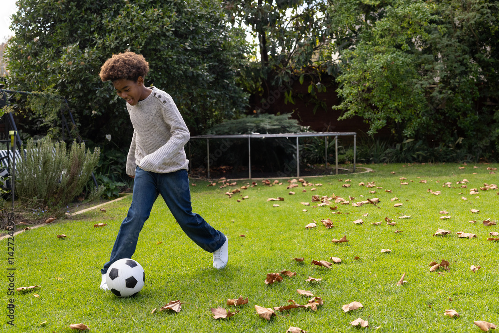 Boy kicking black and white soccer ball in backyard, with trampoline and fallen leaves, copy space Boy kicking black and white soccer ball in backyard, with trampoline and fallen leaves, copy space