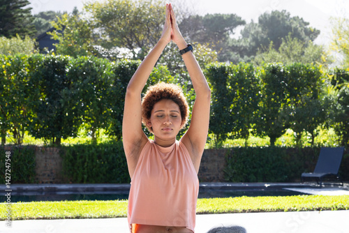 Woman stretching in yoga pose by pool in backyard, wearing fitness watch and enjoying sunshine