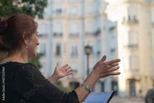 Schilderij op canvas Mature woman with outstretched arms singing outdoors, accompanied by a music stand