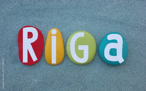 Riga, capital and largest city of Latvia, creative souvenir or logo composed with multi colored hand painted stone letters over green sand