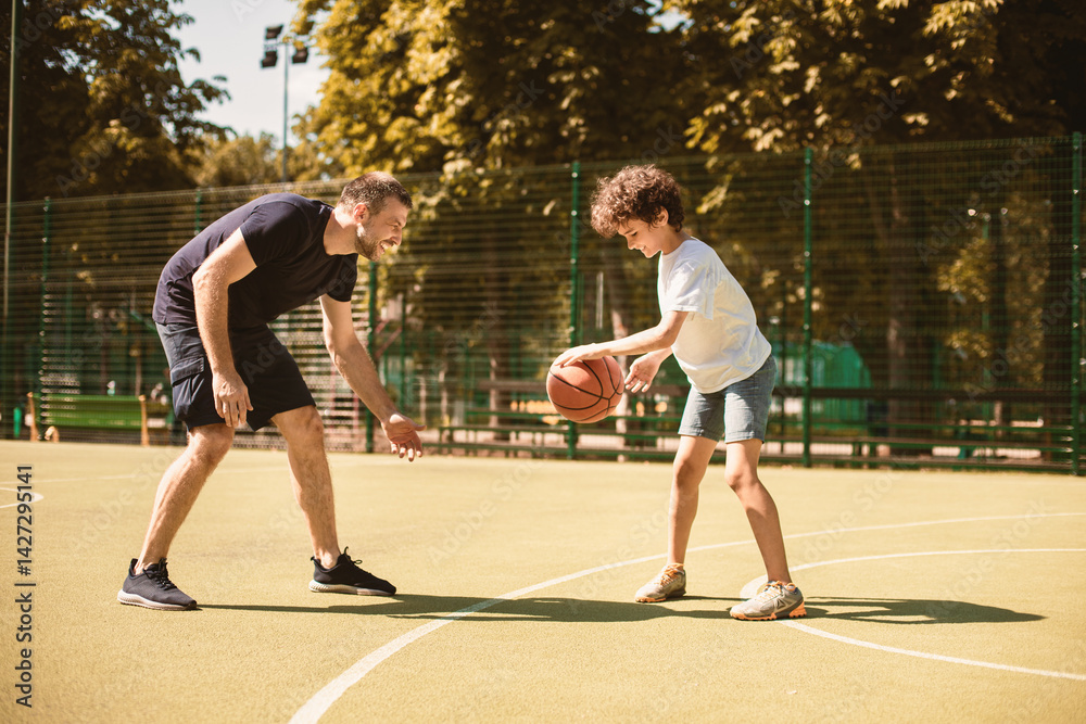Obraz premium Sports Concept. Side view portrait in action of man and boy playing basketball together on the field