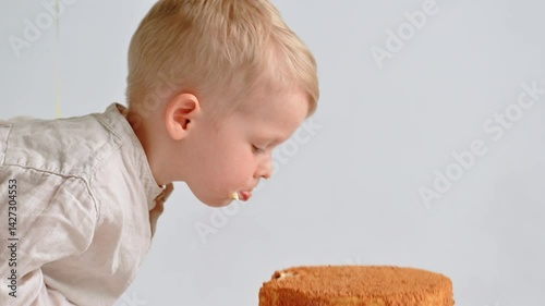 Three-year-old boy bites birthday cake and smiles against a clean white indoor backdrop, capturing a joyful, sweet celebration moment.
