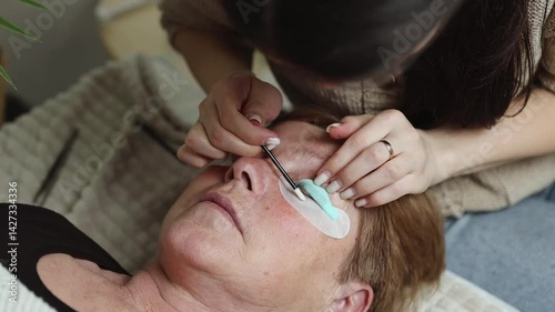 A girl cosmetologist laminates the eyelashes of a senior woman.