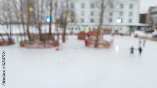 Winter ice rink blurred motion with skating people in urban park setting.