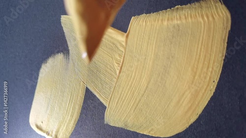 Closeup artistic brushstroke painting in glossy gold acrylic on dark canvas surface.
