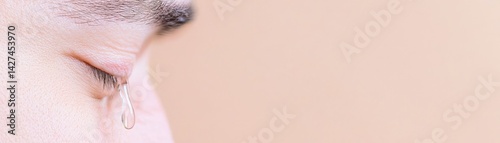 A close-up of a person's eye with a single tear, depicting emotion and vulnerability against a soft, muted background.
