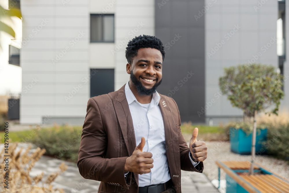 Portrait of smiling african american businessman standing at business center outdoor and giving thumbs up at camera.