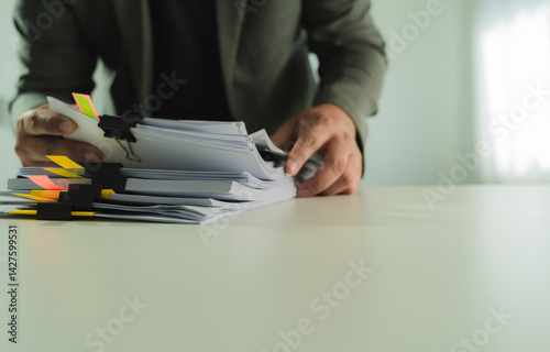 Obraz na płótnie Stacks of paper files and checking document businessman checks financial documents on his laptop, managing corporate reports and legal paperwork at his office desk. w salonie